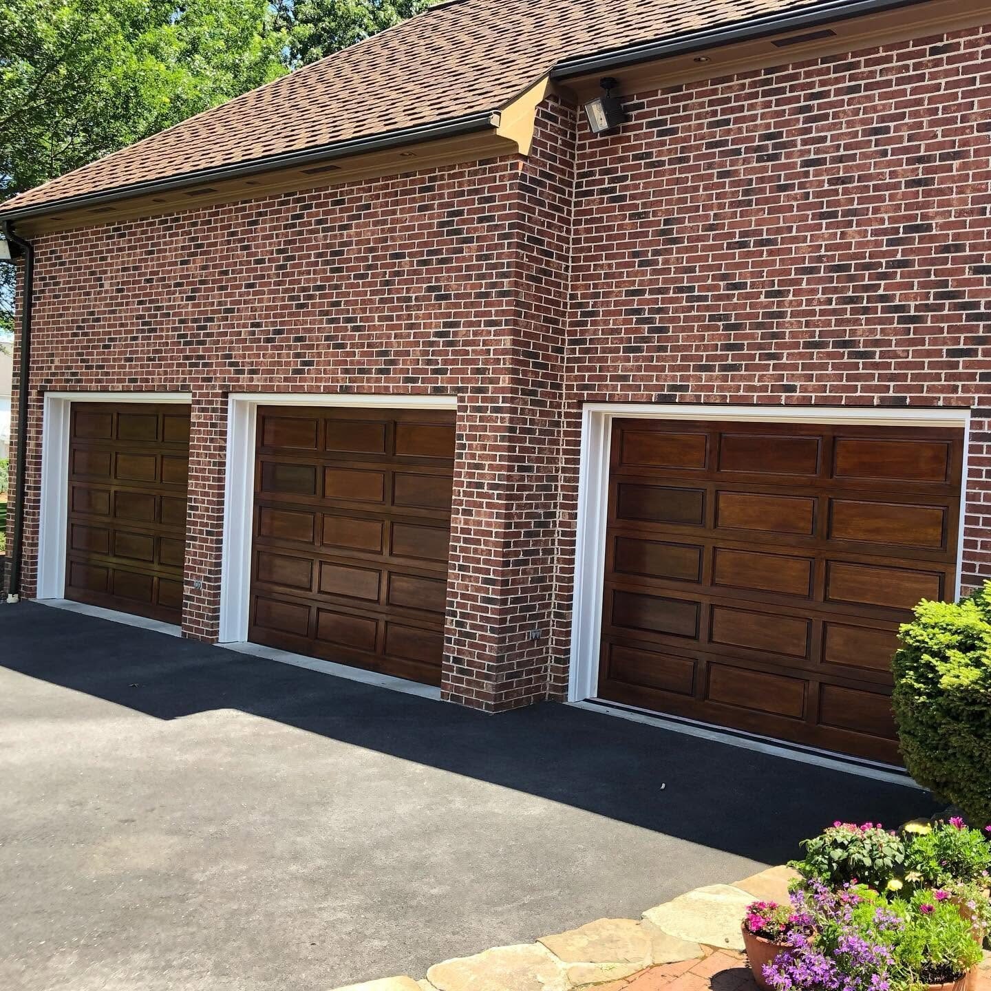 Three stained wood garage doors on a brick garage